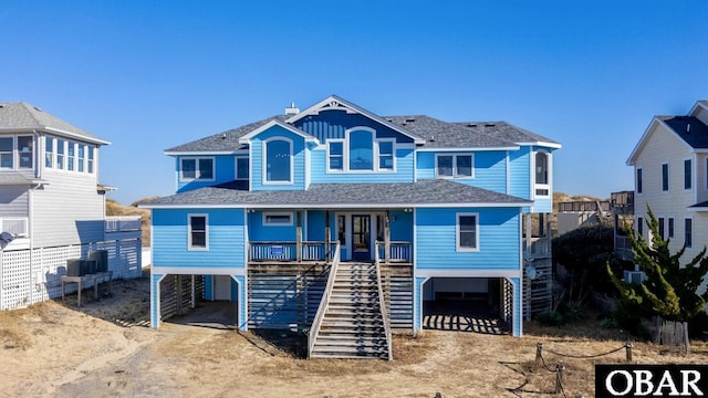 coastal home with dirt driveway, a carport, a porch, and roof with shingles