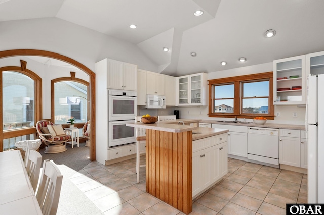 kitchen featuring white appliances, white cabinets, light countertops, a center island, and glass insert cabinets