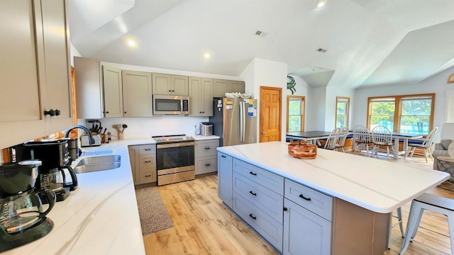 kitchen with a kitchen breakfast bar, vaulted ceiling, light countertops, appliances with stainless steel finishes, and a center island