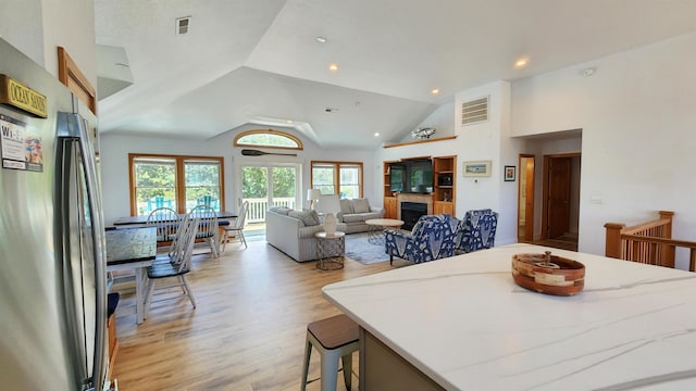 interior space with a fireplace, light wood finished floors, lofted ceiling, recessed lighting, and visible vents