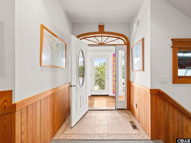 foyer entrance with a wainscoted wall, visible vents, and wooden walls