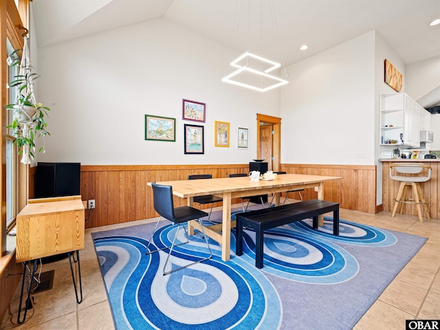dining space with vaulted ceiling, wainscoting, wood walls, and light tile patterned floors