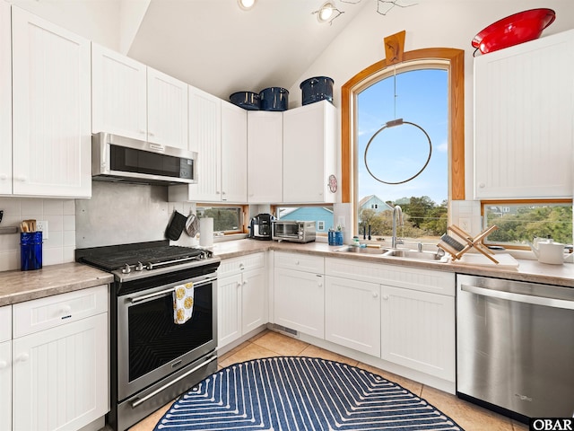 kitchen featuring vaulted ceiling, light countertops, backsplash, a sink, and stainless steel appliances
