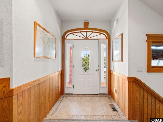 foyer entrance featuring wainscoting, light tile patterned flooring, wood walls, and visible vents