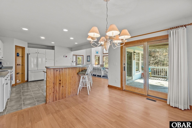 kitchen with white cabinets, visible vents, light wood finished floors, and white fridge