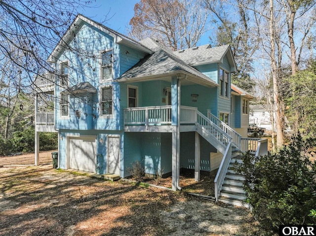 view of front facade with dirt driveway, stairway, covered porch, and a garage