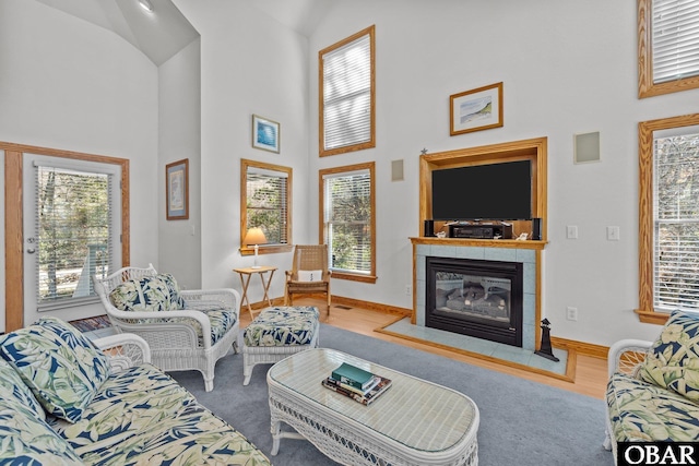 living area featuring a high ceiling, a fireplace, wood finished floors, and baseboards