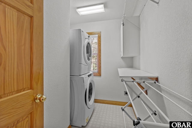 laundry room featuring light floors, a textured wall, stacked washer / dryer, laundry area, and baseboards