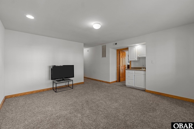 carpeted living room with baseboards, visible vents, and a sink