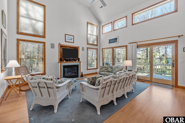 living area with a fireplace, a ceiling fan, wood finished floors, high vaulted ceiling, and baseboards