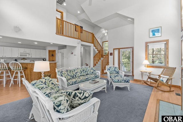 living room with light wood-type flooring, visible vents, stairs, and high vaulted ceiling