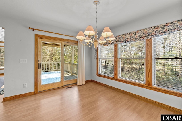 unfurnished dining area featuring light wood-type flooring, an inviting chandelier, baseboards, and visible vents