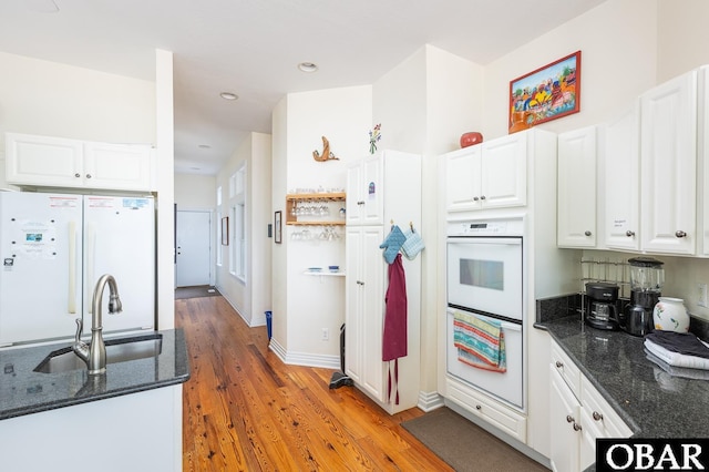 kitchen with white cabinets, a sink, dark stone countertops, and white appliances