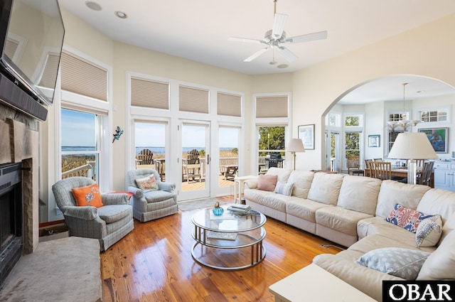 living area featuring a tiled fireplace, hardwood / wood-style flooring, ceiling fan, arched walkways, and a towering ceiling