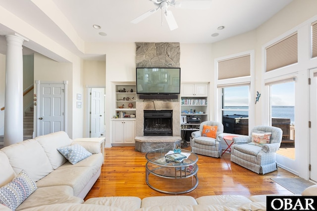 living room with stairs, a fireplace, light wood-style flooring, and a ceiling fan
