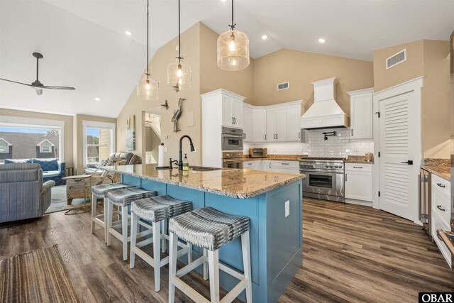 kitchen featuring white cabinetry, appliances with stainless steel finishes, custom exhaust hood, and open floor plan