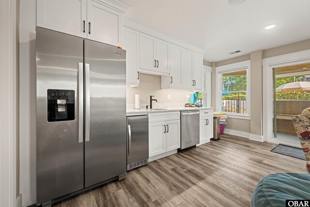 kitchen with visible vents, white cabinets, stainless steel appliances, light wood-style floors, and a sink