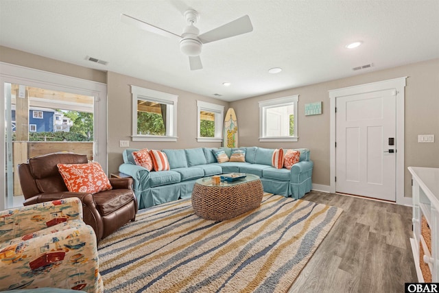 living area featuring a textured ceiling, light wood-type flooring, visible vents, and baseboards