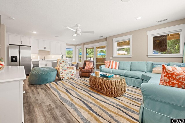 living room featuring light wood-type flooring, visible vents, a ceiling fan, and recessed lighting