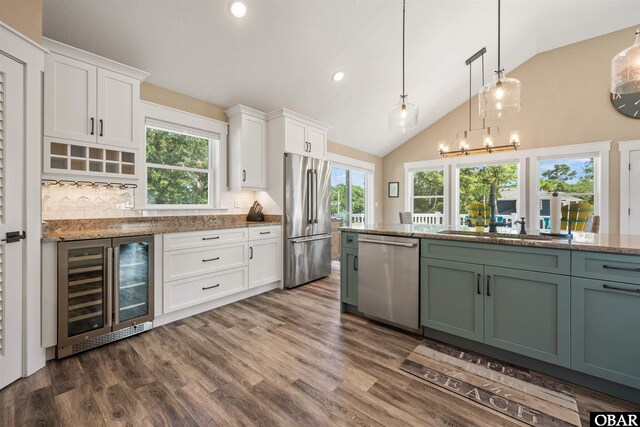 kitchen featuring beverage cooler, dark wood finished floors, appliances with stainless steel finishes, hanging light fixtures, and white cabinetry