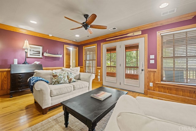 living area with light wood-style floors, a wainscoted wall, visible vents, and crown molding