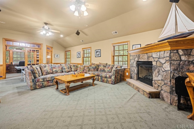 carpeted living area featuring lofted ceiling, a stone fireplace, visible vents, a ceiling fan, and wainscoting