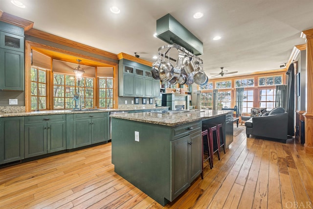 kitchen with glass insert cabinets, a center island, green cabinetry, and light stone counters