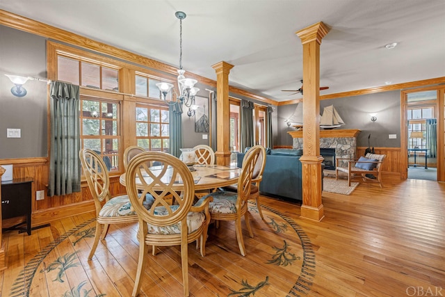 dining area featuring a wainscoted wall, ornamental molding, light wood-style flooring, and decorative columns