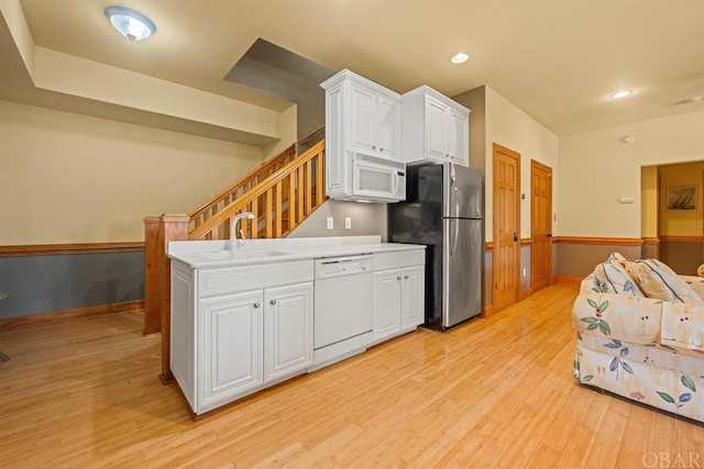 kitchen featuring light countertops, white cabinetry, a sink, light wood-type flooring, and white appliances