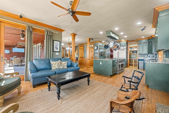 living area featuring a ceiling fan, decorative columns, light wood finished floors, and ornamental molding