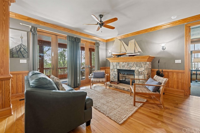 living area featuring light wood-style flooring, a fireplace, crown molding, and wainscoting