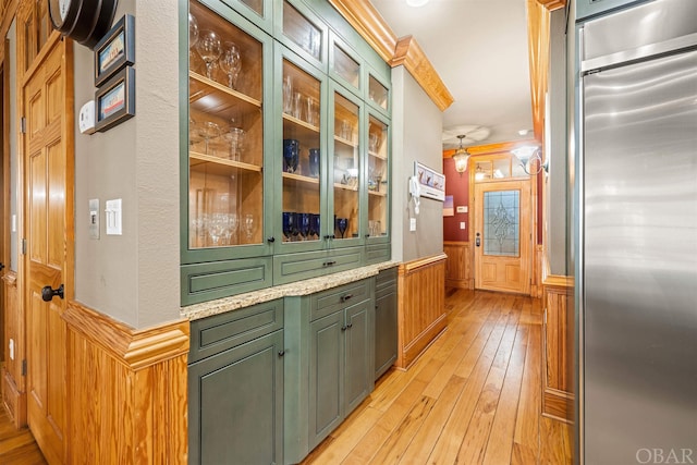 kitchen with light stone counters, a wainscoted wall, light wood finished floors, glass insert cabinets, and stainless steel built in fridge