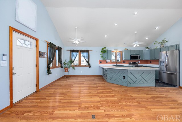 kitchen featuring a peninsula, stainless steel appliances, a sink, light wood-style floors, and light countertops