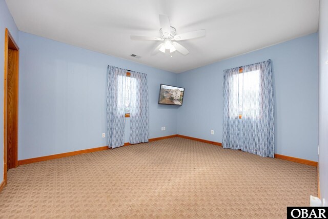 carpeted spare room featuring a wealth of natural light, visible vents, ceiling fan, and baseboards