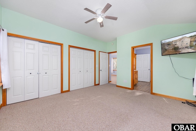 unfurnished bedroom with carpet floors, two closets, lofted ceiling, ceiling fan, and baseboards