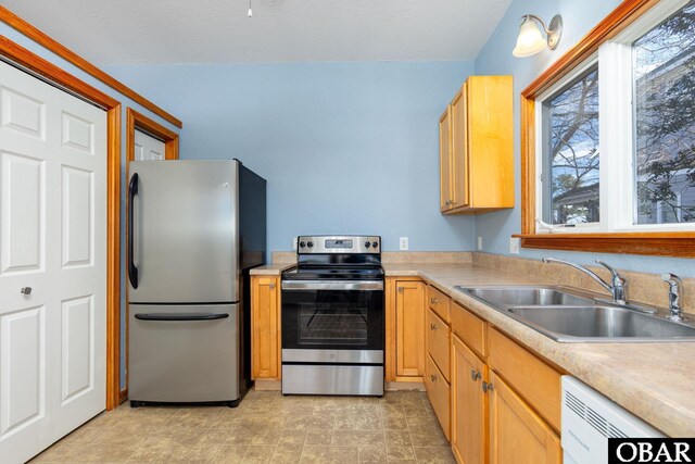 kitchen featuring appliances with stainless steel finishes, light countertops, a sink, and light brown cabinetry