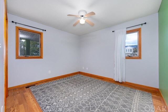 spare room featuring wood finished floors, a ceiling fan, and baseboards