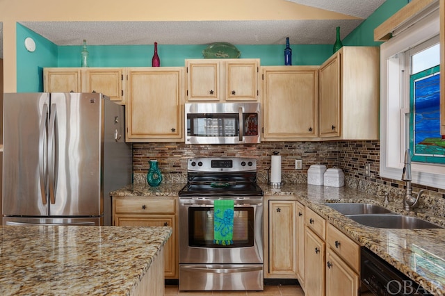 kitchen with light brown cabinets, light stone counters, stainless steel appliances, and a sink