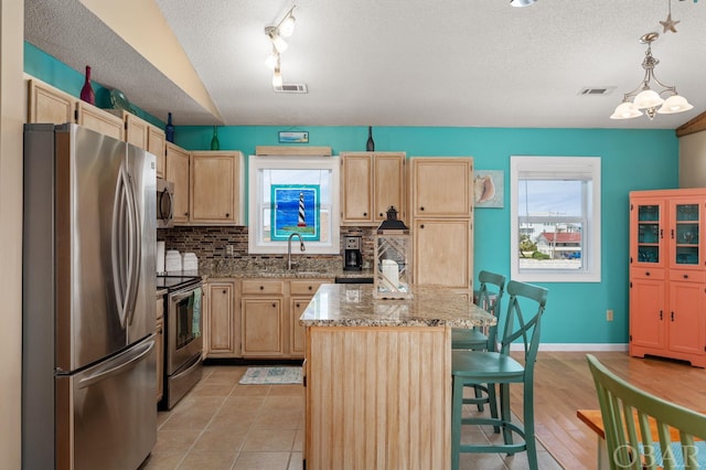 kitchen with a center island, pendant lighting, a breakfast bar area, appliances with stainless steel finishes, and light stone countertops