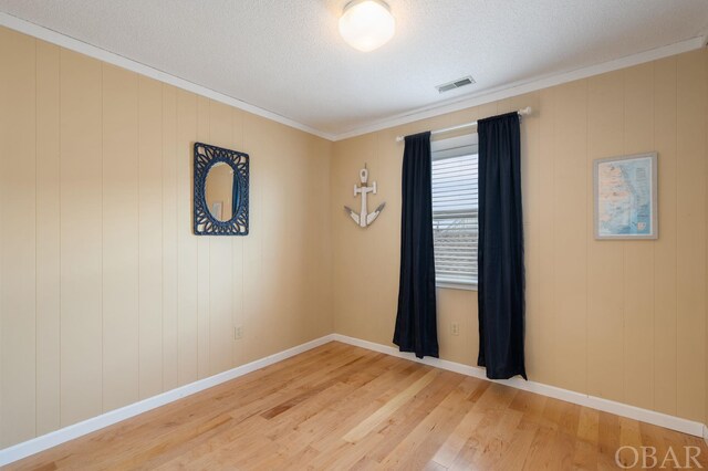 empty room featuring crown molding, visible vents, a textured ceiling, wood finished floors, and baseboards