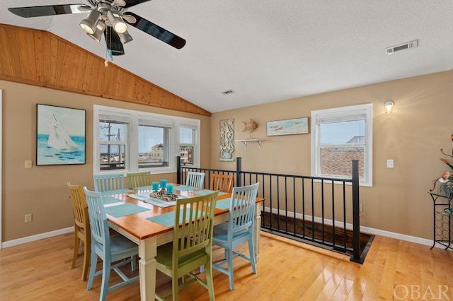 dining space featuring light wood-style floors, plenty of natural light, visible vents, and vaulted ceiling