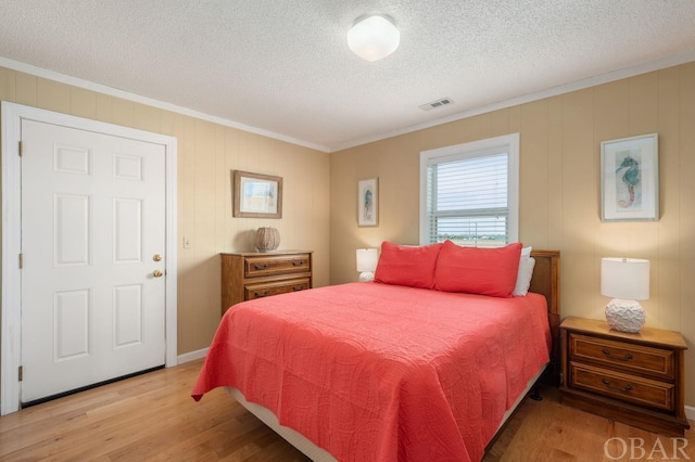 bedroom with light wood-style flooring, visible vents, a textured ceiling, and ornamental molding