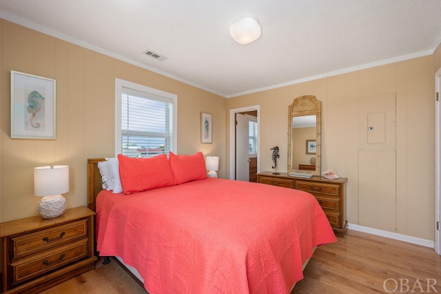 bedroom with light wood finished floors, visible vents, and crown molding