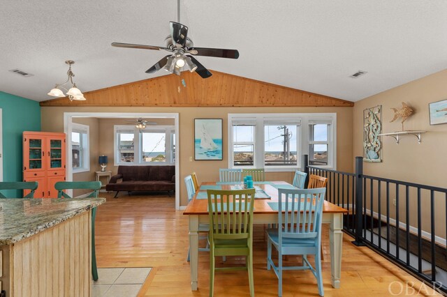 dining room featuring lofted ceiling, light wood finished floors, visible vents, and a textured ceiling