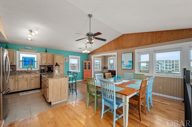 dining area featuring baseboards, a ceiling fan, lofted ceiling, light wood-style flooring, and a textured ceiling