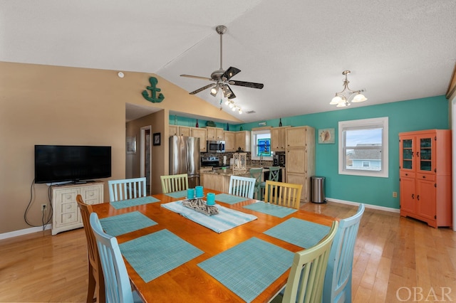 dining space with lofted ceiling, light wood finished floors, ceiling fan with notable chandelier, and baseboards