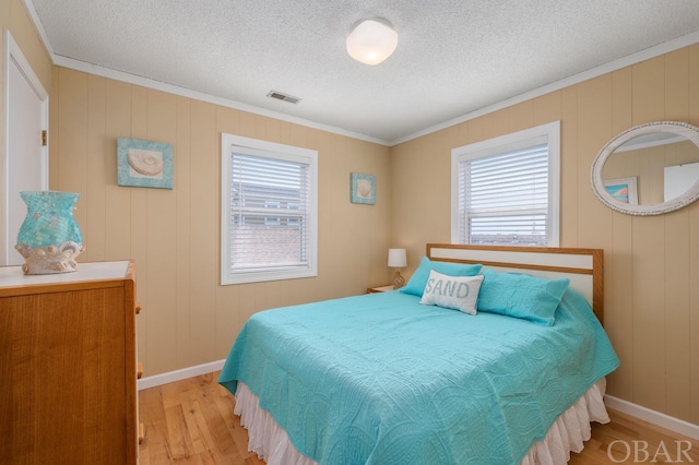 bedroom with visible vents, light wood-style floors, ornamental molding, a textured ceiling, and baseboards