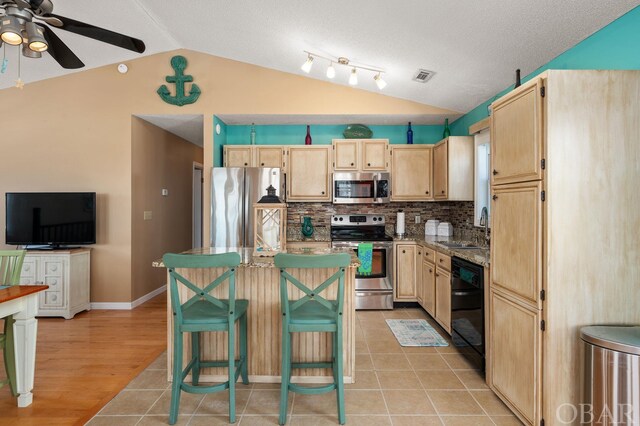 kitchen with a breakfast bar, stainless steel appliances, light brown cabinets, vaulted ceiling, and a sink