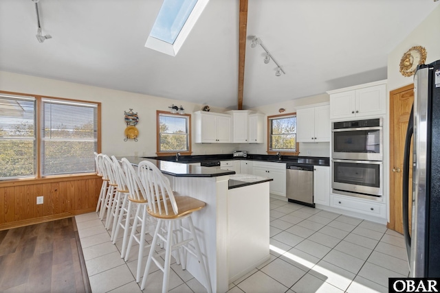 kitchen with appliances with stainless steel finishes, white cabinets, wooden walls, a peninsula, and a kitchen bar