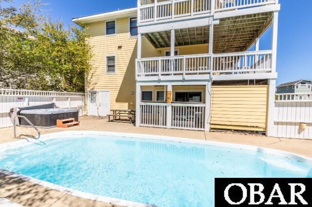 rear view of property with a balcony, a hot tub, and fence